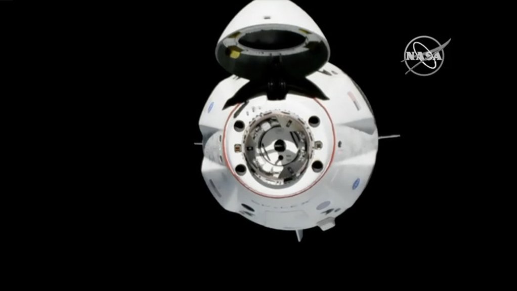 The CrewDragon space capsule about to dock with the International Space Station, with its nose cone open, revealing docking attachment points and the crew transfer hatch