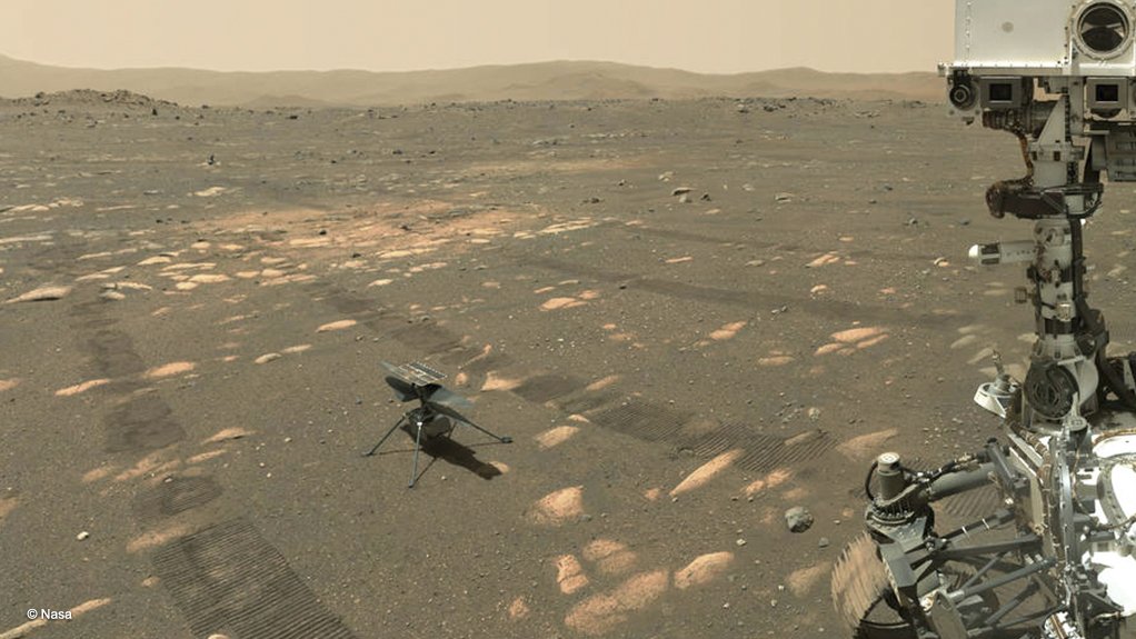 The Ingenuity drone helicopter (centre-left) sitting on the Martian surface, photographed by the Perseverance rover (part of which is visible on the right)