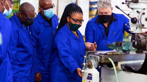 A photo young black men and women being trained by an older white man in an automotive component manufacturing facility