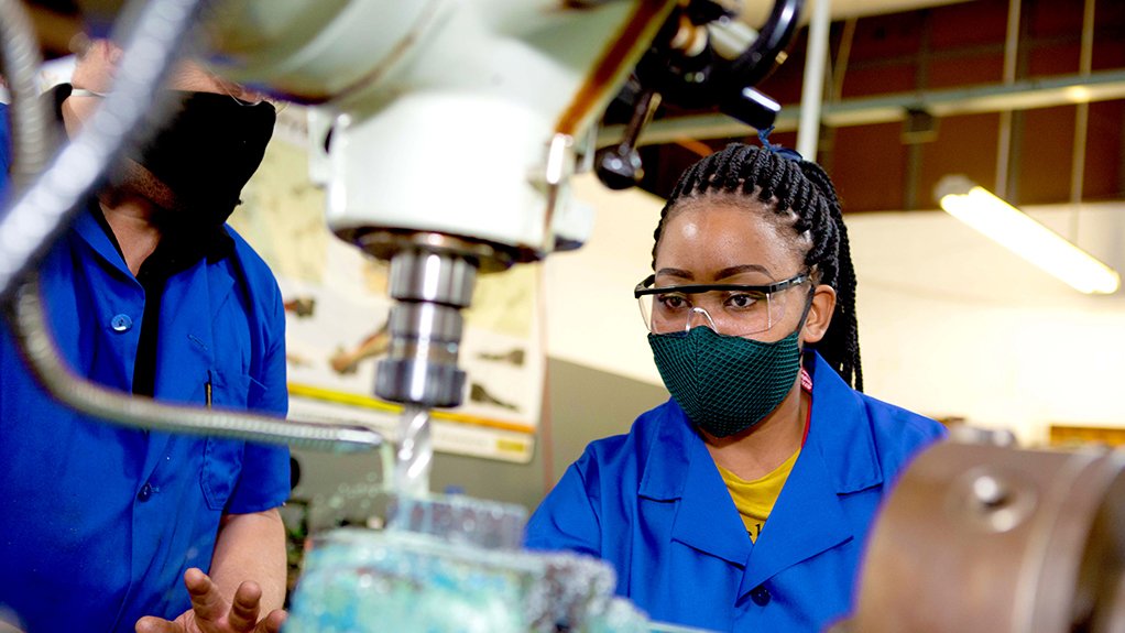 A photo young black woman operating machinery under supervision in an automotive component manufacturing facility