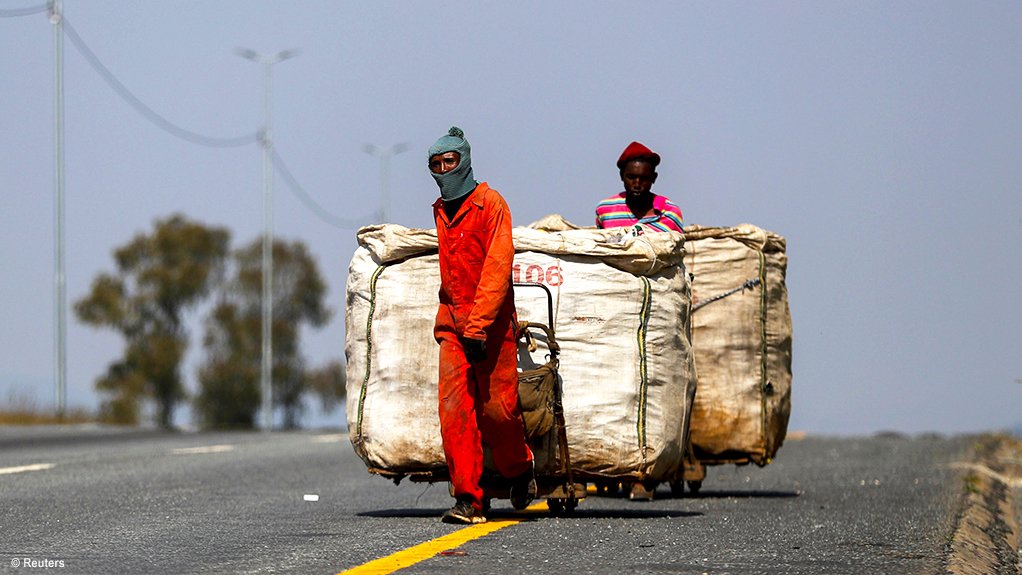 A photo of two informal waste reclaimers walking along the road dragging trolleys laden with recyclable waste