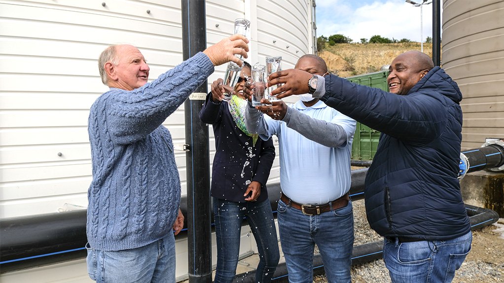 A photo of four people outside toasting one another with glasses of clean water at a water processing plant