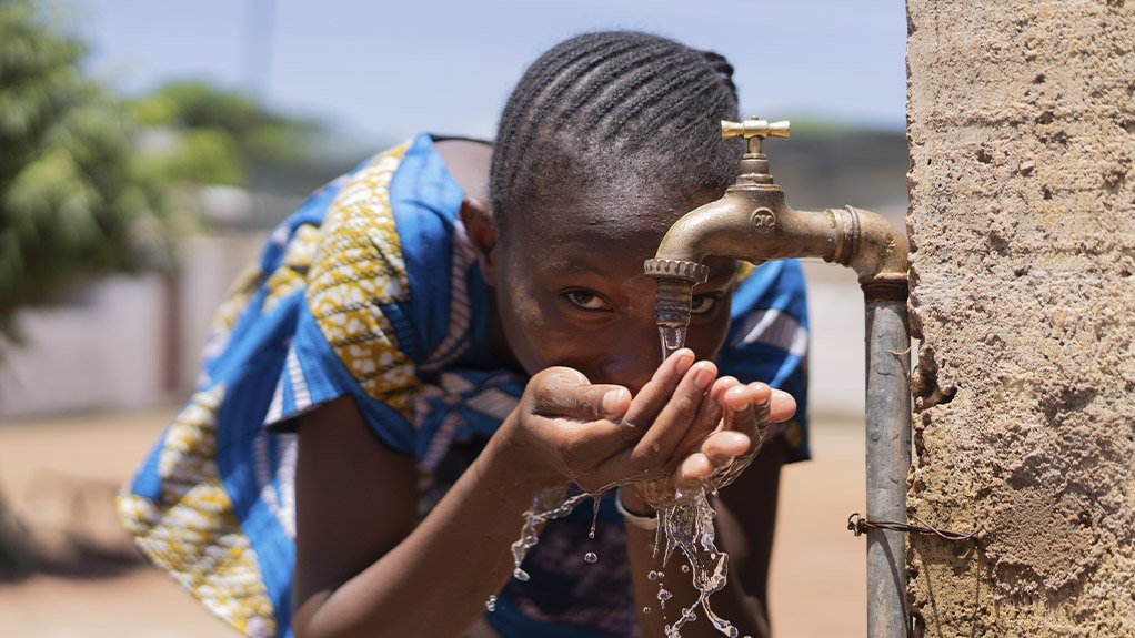 A photo of a young girl drinking water from a tap