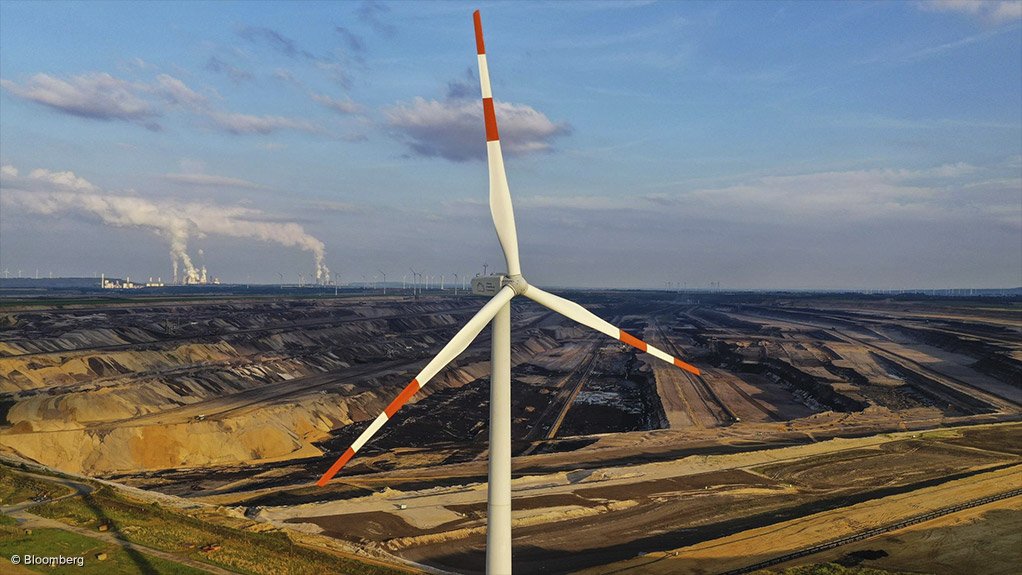 Image of a wind turbine with a coal mine and power station in the background.
