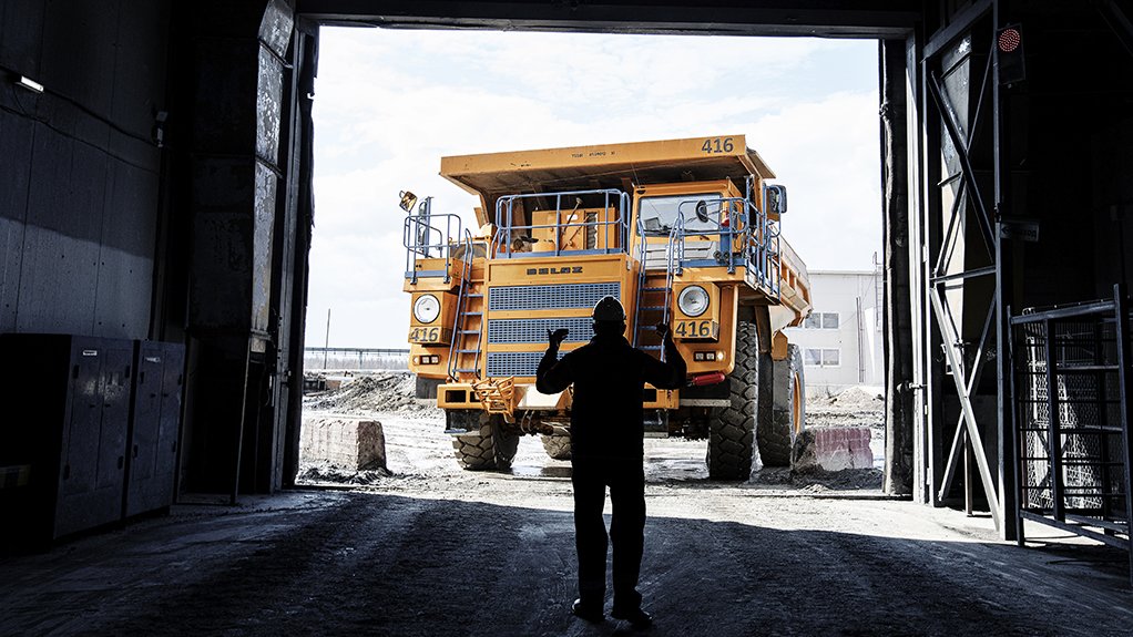 A large yellow mine load dump haul truck entering a mine being directed by a miner at the Russian diamond producer Alrosa operations