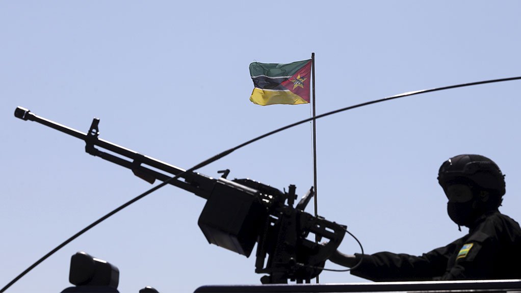 A photo of a Rwandan soldier holding a machine gun atop an armoured personnel carrier with the Mozambique flag in the background