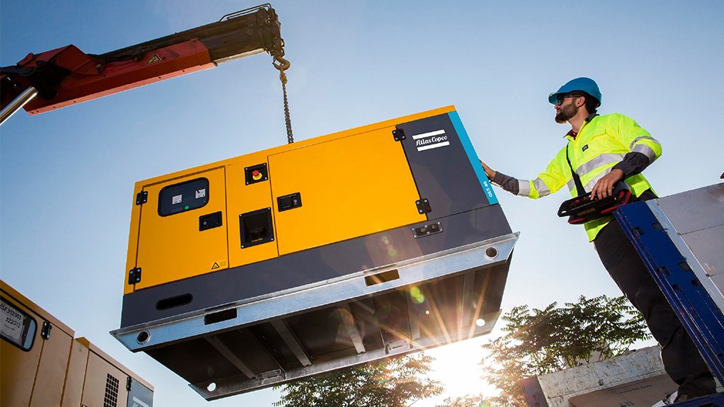 A photo of an Atlas Copco QES genset being lowered by crane and guided by a worker in PPE