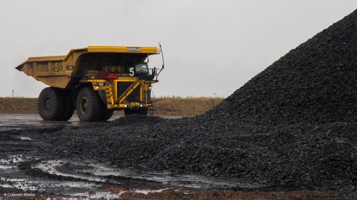 A photo of a dump truck in front of a coal stockpile