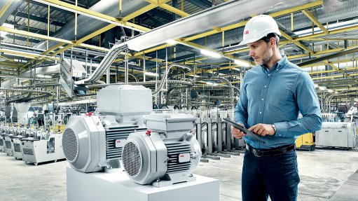 A photo of a technician holding a tablet and working with an ABB motor inside of a factory