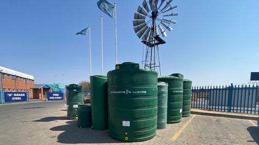 Various green water tanks lined up inside a parking lot with flags waving behind at the Syewarts & Lloyds assembly plant