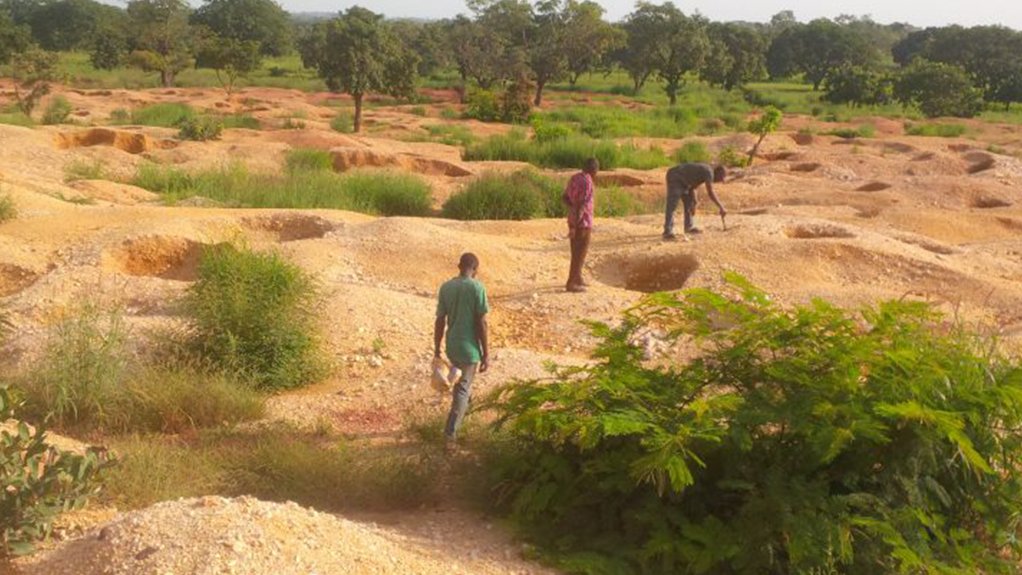 Burkina Faso landscape with many small artisanal holes dug into the ground with artisinal miners milling around