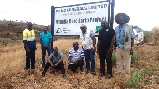 A group of men stood at a sign which says Peak Rare Earths at Ngualla rare earths project in Tanzanid
