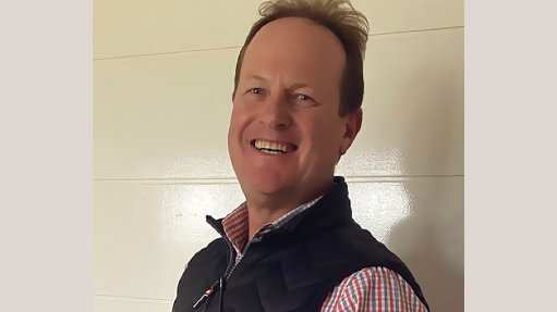 An image depicting a smiling man wearing a red shirt and black vest