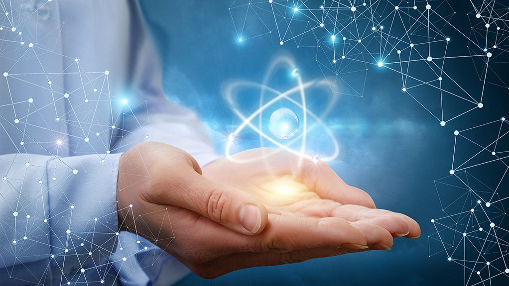 An image depicting a hand holding an atom against a blue background