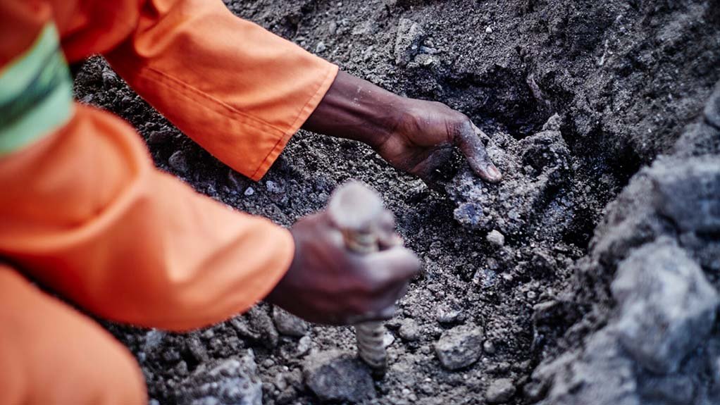 An image of a miner bending to lift a rock 