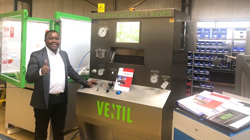 Image depicting a man, Moeketsi Mpotu, wearing a black and white suit, standing in front of a Ventil safety valve testing machine