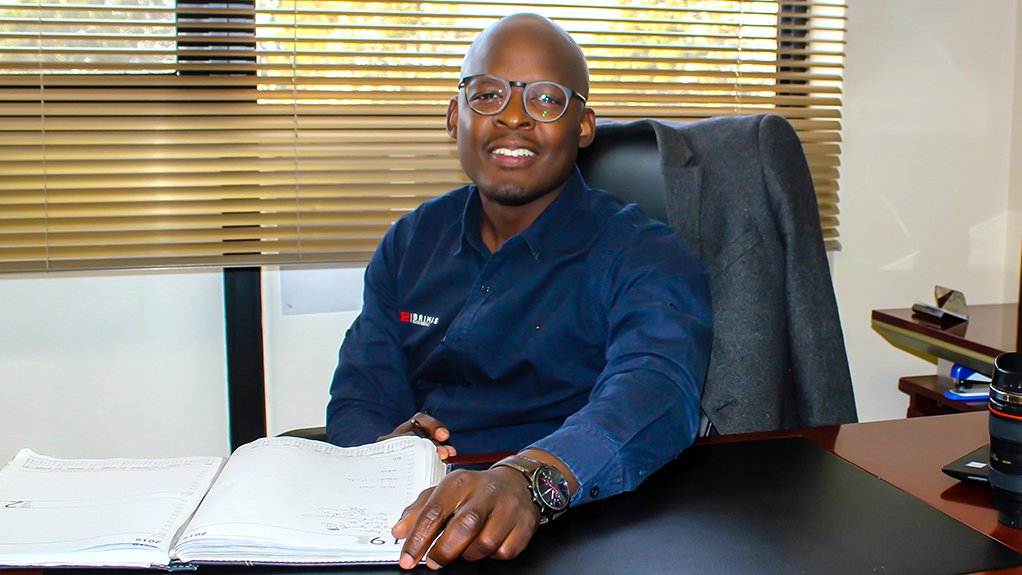 An image depicting a smiling man, Andile Nqandela, sitting at a desk