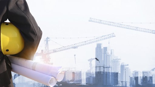 Image depicting a person holding a yellow construction helmet and plans against a blue and white construction site backdrop 