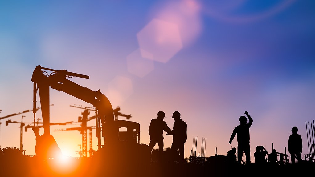 An image depicting a silhouette of construction workers and an excavator against the backdrop of a blue and yellow sunset