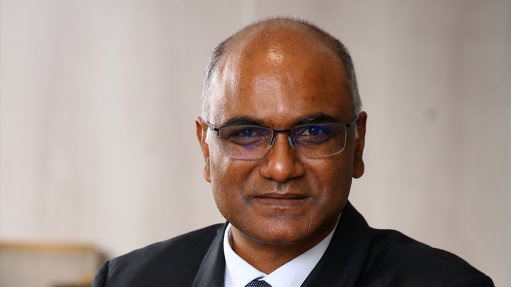 An image of Vis Reddy wearing a black and white suit and glasses standing with his arms crossed