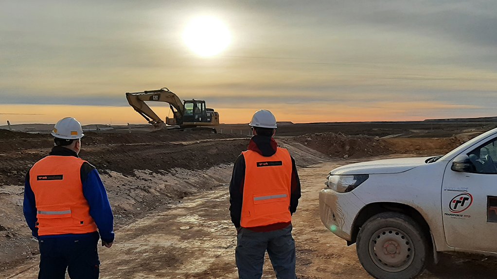 An image depicting two consulting engineers wearing bright orange vests and hard hats overlooking a mine site, standing next to a white vehicle