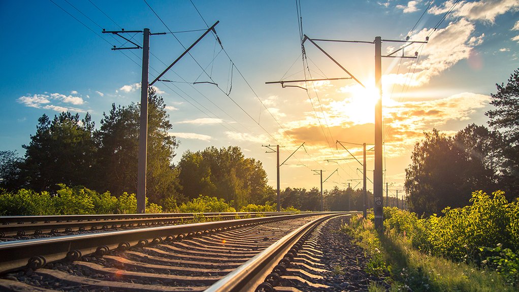 An image depicting railway tracks against the backdrop of a blue sky with white clouds and a bright shining sun