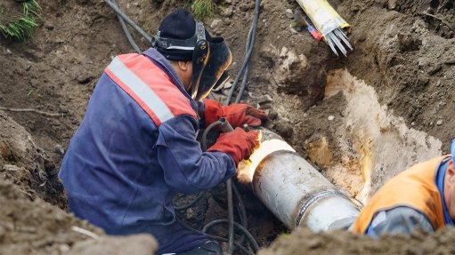A man in a ditch welding a water pipe out in the open, which would be inaccessible to a robotic welder