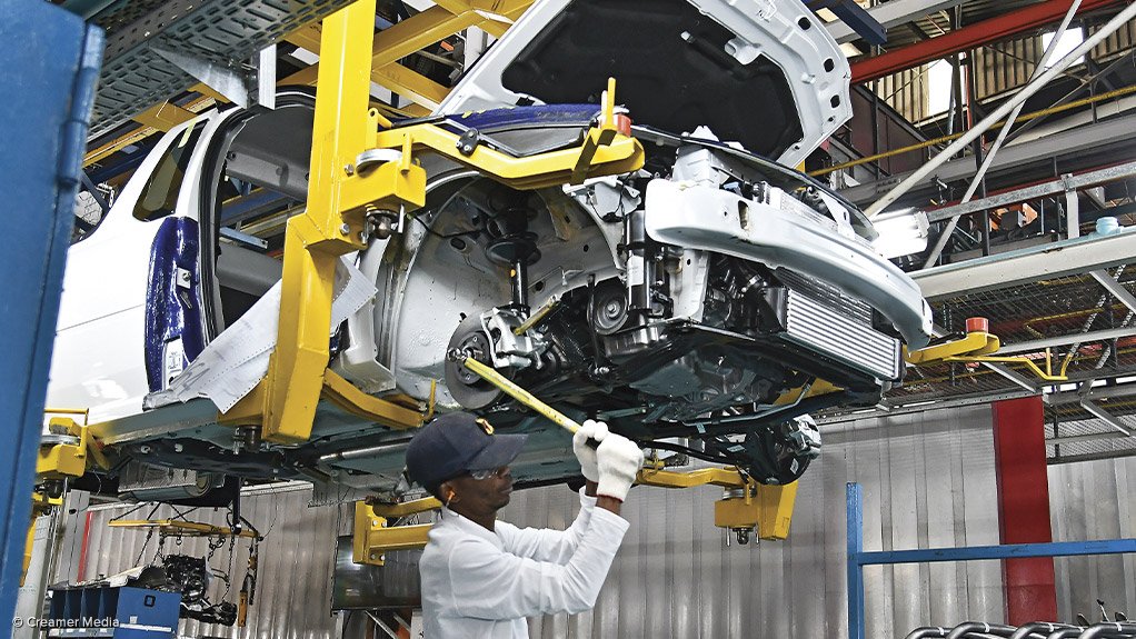 A vehicle in the manufacturing process hoisted up on a lift with a worker stood under the chassis