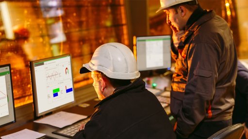 A picture of two gentlemen with hard hats sat at a station with three screens in front of them displaying telemetry data and statistics