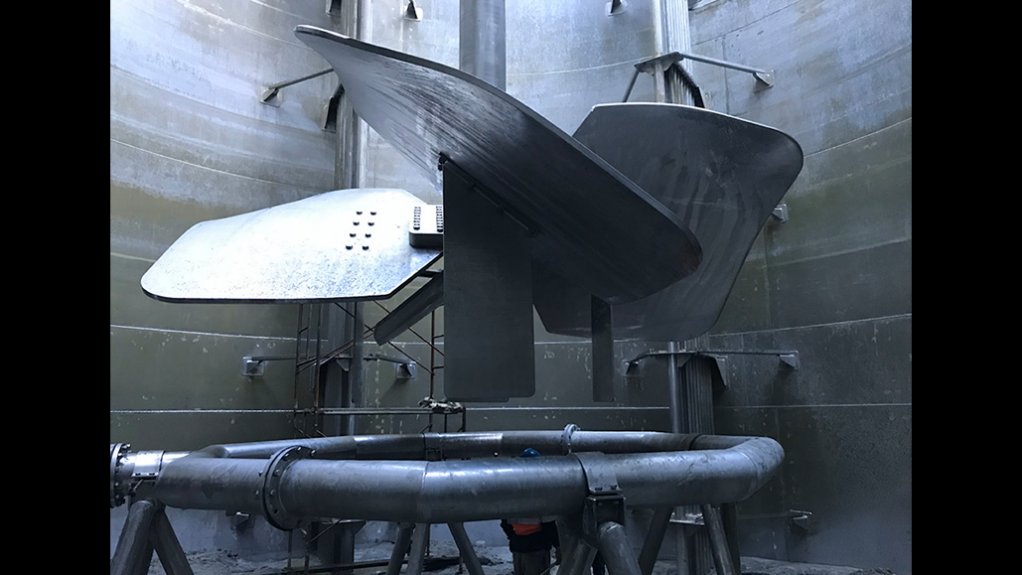 A large agitator propeller installed inside a tank, with a man under the blades checking them. 