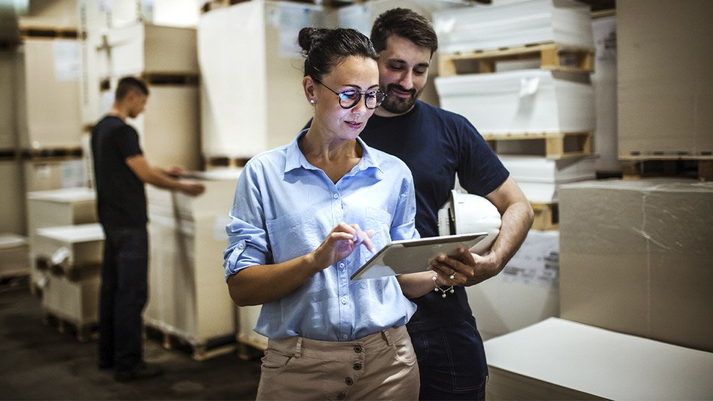 A woman holding a tablet wearing glasses working with a man looking at the tablet, in a warehouse environment