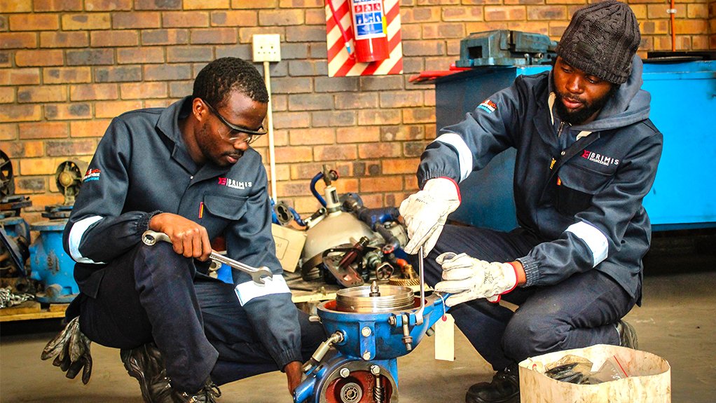 Two workers assembling a valve on the floor, wearing PPE and using hand held tools