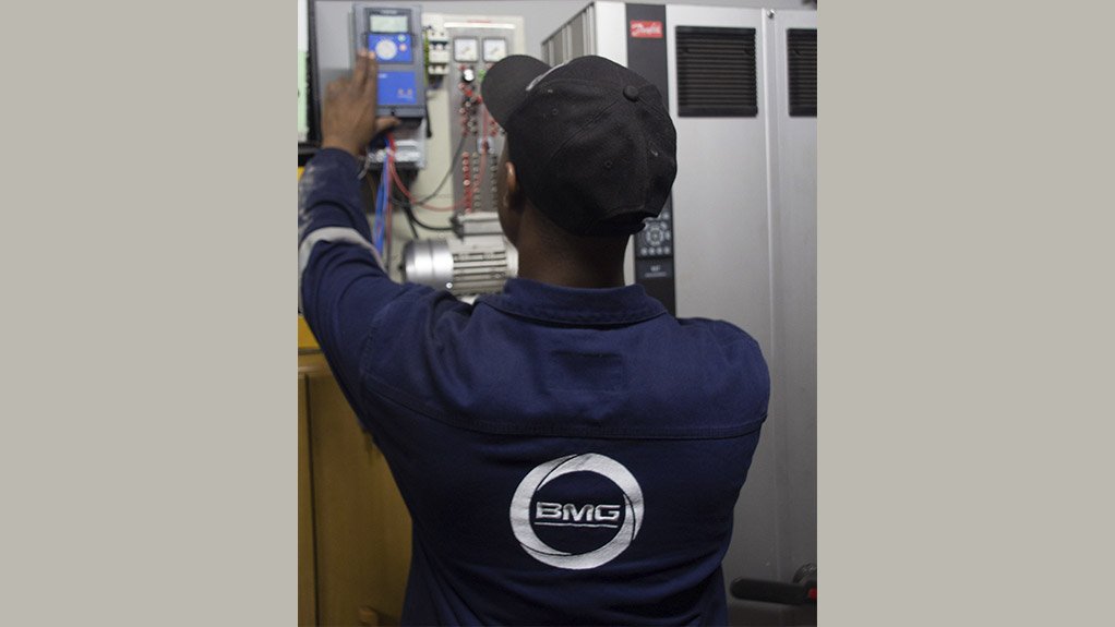 A man wearing a  blue overall with the BMG logo on servicing a Danfoss drive