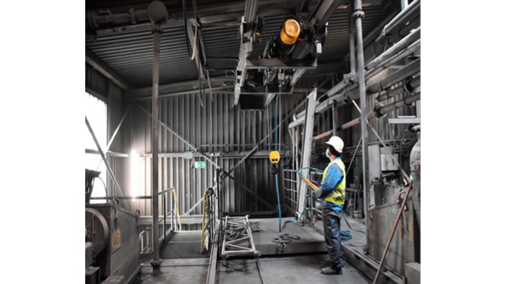 Man with white hard hat operating Kito RX wire rope hoist in an industrial plant.