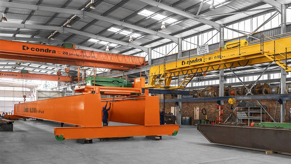 Condra crane manufacturing facility in Germiston where orange and yellow painted cranes are being assembled by factory workers.