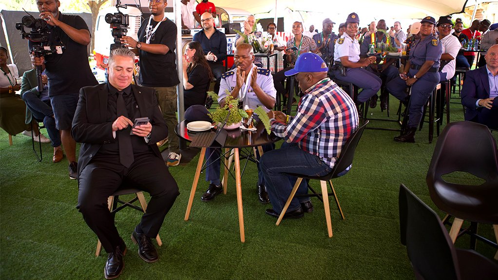 Burton Swain siting in the middle of the crowd in front of a mobile DJ box and members of the SAPS, at the revamped The Spot 1818 Tavern in Soweto