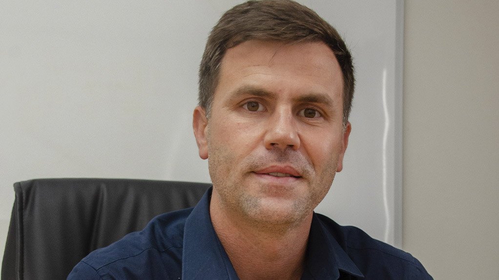 Kobus van den Berg sitting at a desk, navy shirt, hands clasped in front of him.