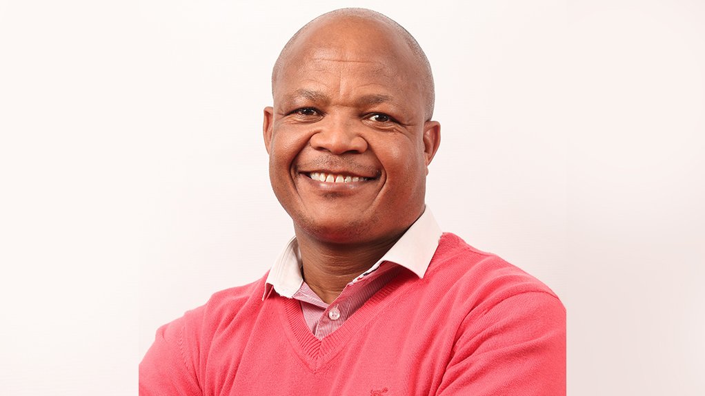 Photo of Stoffel Molokwane, smiling, arms crossed, red jumper, collared shirt.