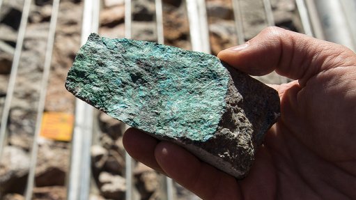 a rock made of copper ore being held in a mans hand in front of drilled ore samples.