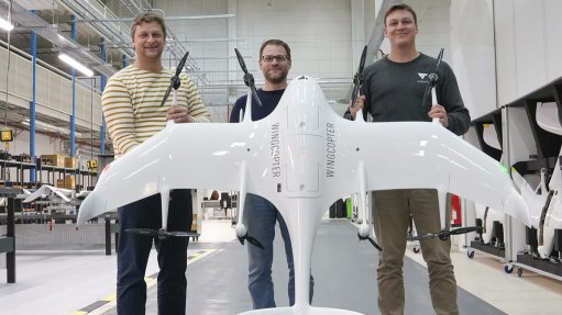3 gents in a facility holding a large white plane like drone