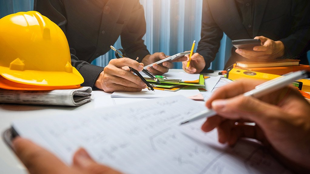 A generic image of a table covered in plans drawings and contracts with male and female hands assessing the pages on the table.