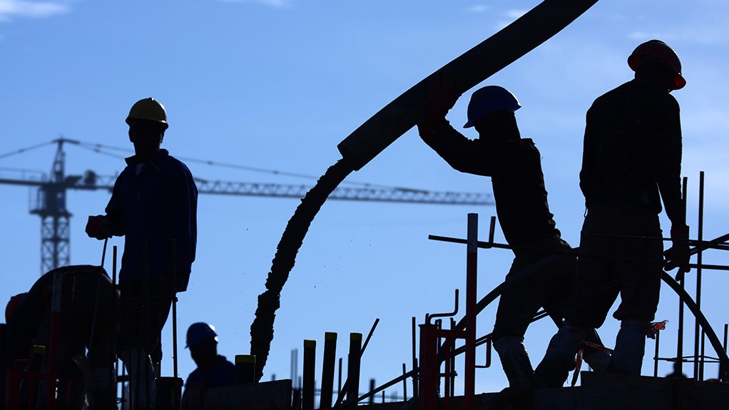 A silhouette of construction workers pouring concrete at a construction site