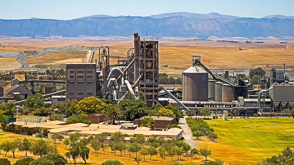 A large cement manufacturing plant with green landscape behind.