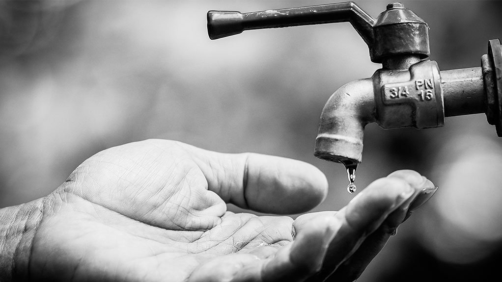 a black and white photo of an adult male hand under a tap with sparse water dripping out if it