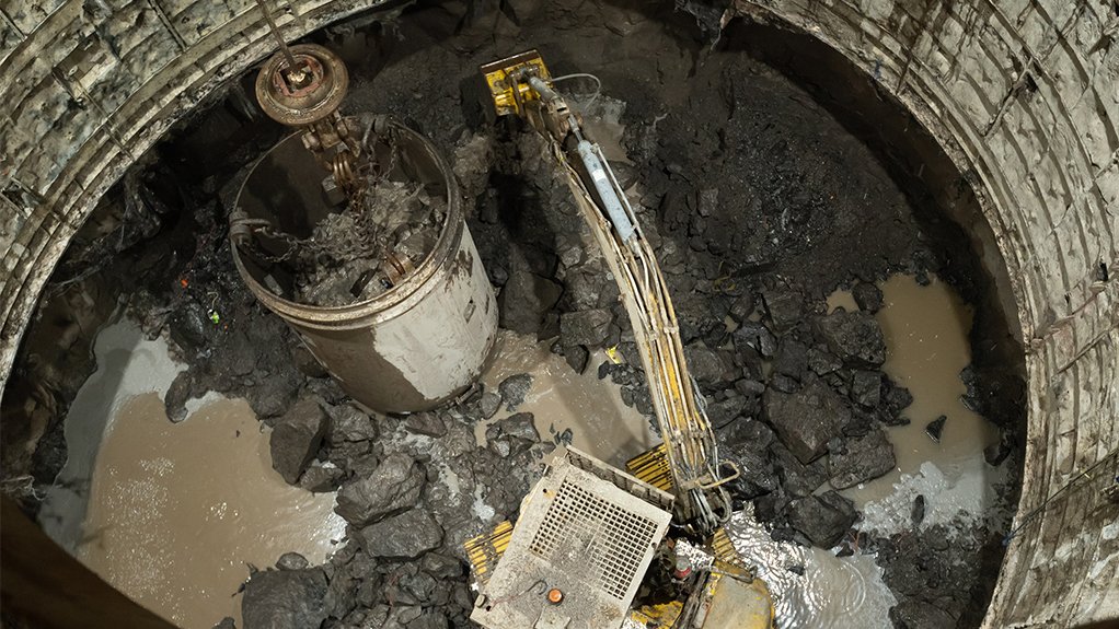 An excavator busy lashing at the shaft bottom with shaft lining being carried out on the face