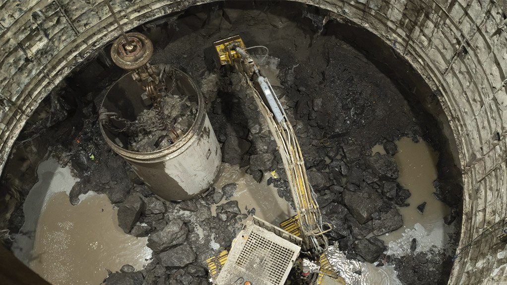 An excavator busy lashing at the shaft bottom with shaft lining being carried out on the face