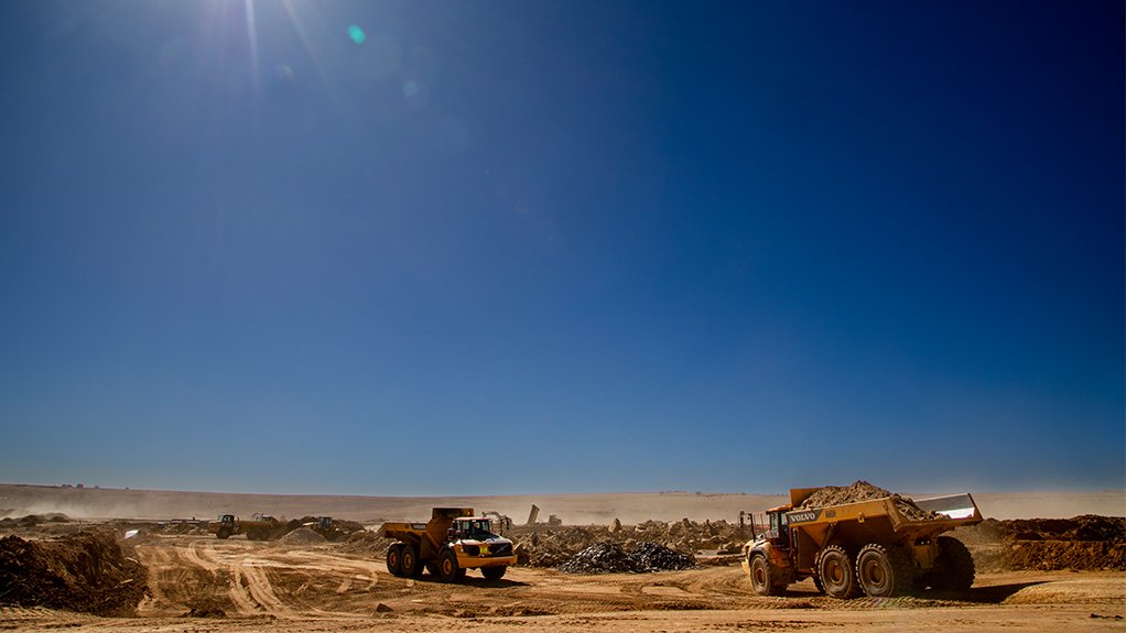 A load haul machine driving in a sparse mining terrain with the sun shining brightly in the sky