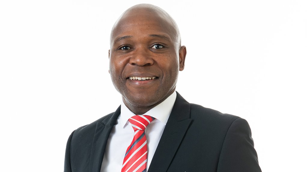 Image of a man dressed in a black suit and a red, white and navy stripped tie