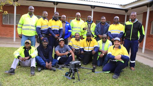 a group of men in PPE in front of a mine building with a drone in front of them
