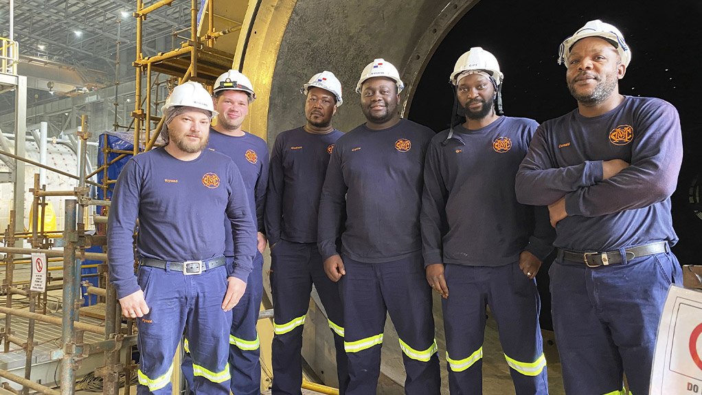 6 men stood in front of a large metal ball mill wearing PPE